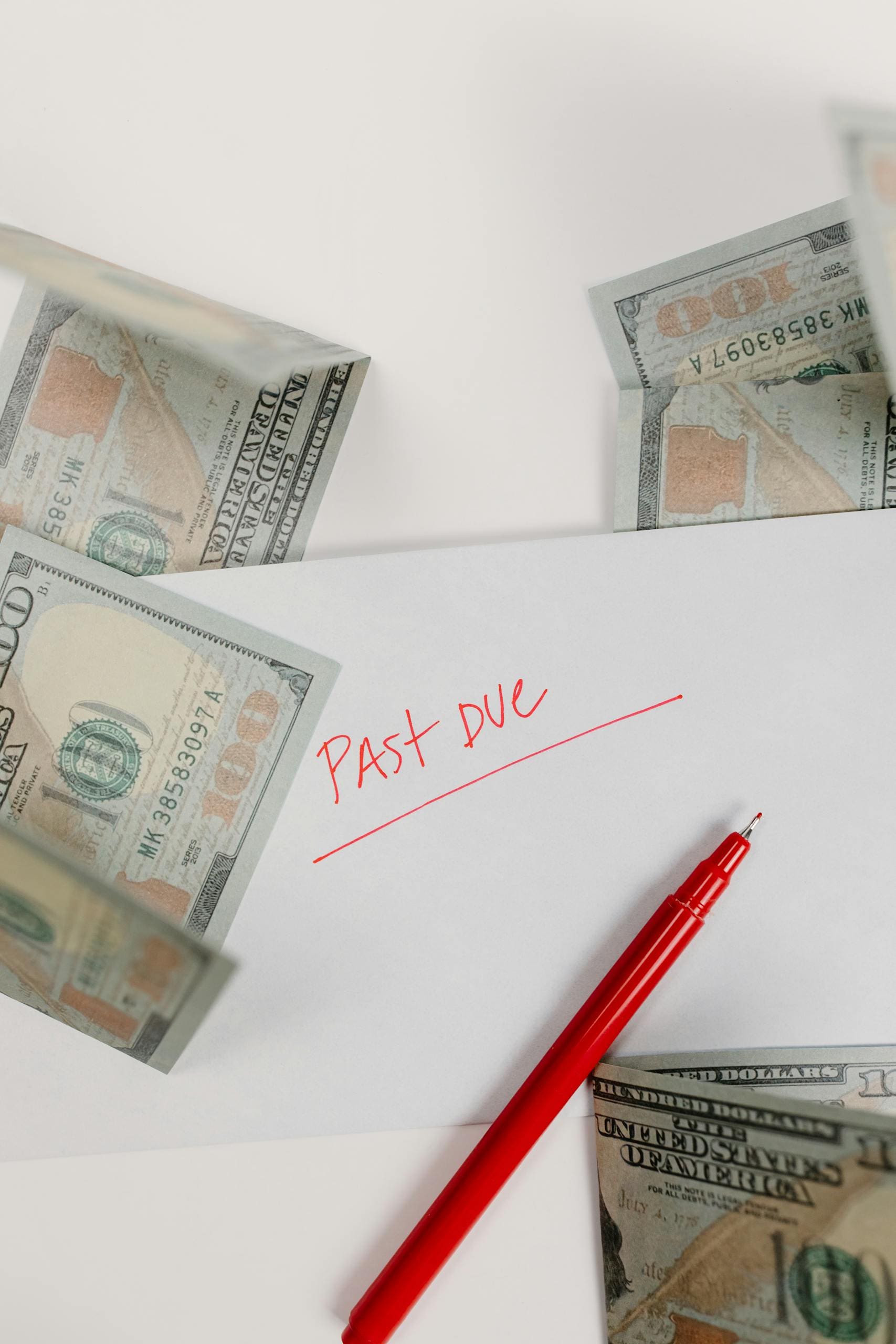 Envelope marked 'Past Due' surrounded by hundred-dollar bills and red pen on white background.