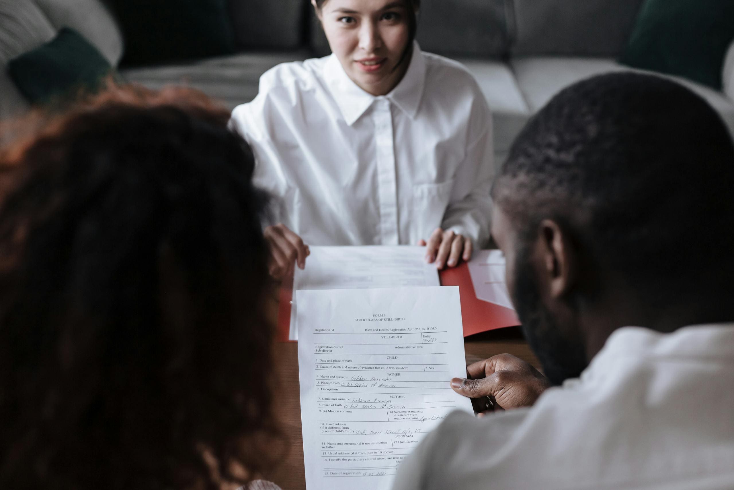 Close-up view of hands signing an adoption form with a pen atop a white table.