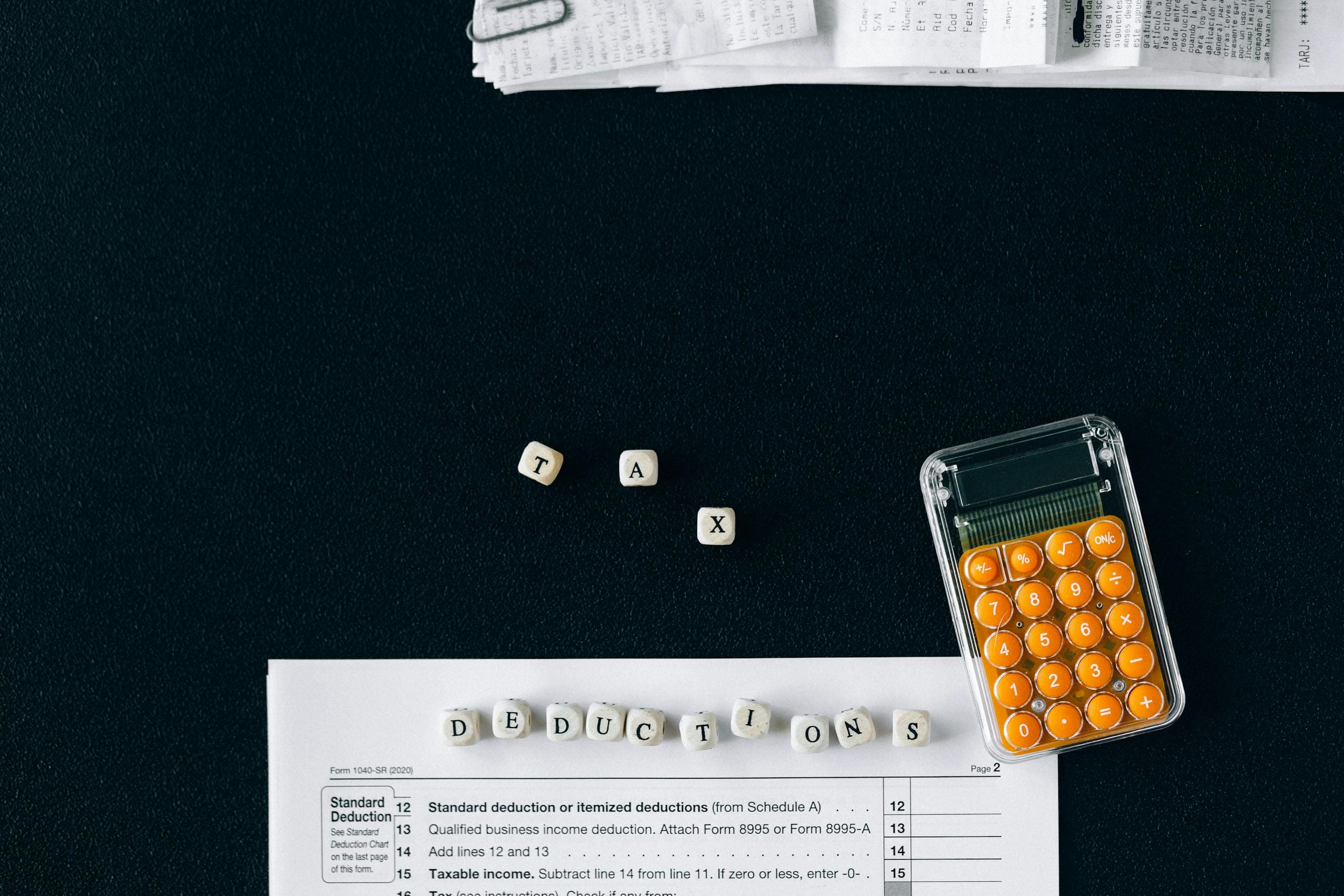 Top-down view of tax deduction items on a black background with a calculator and forms, emphasizing financial planning.